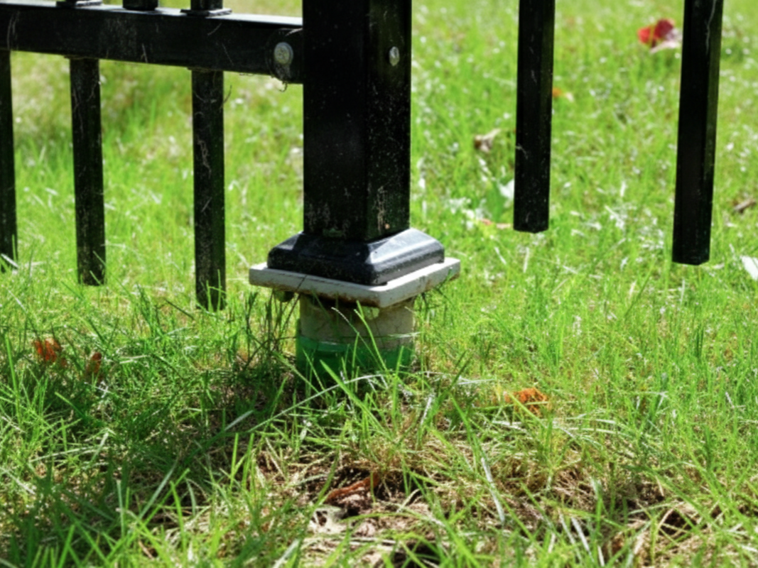 Black metal fence post set in green grass.