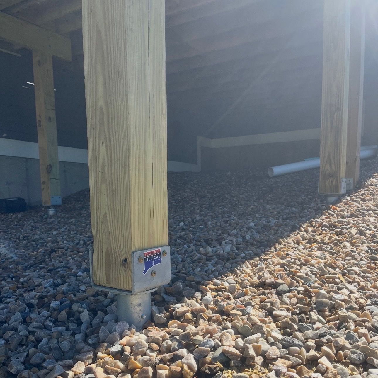 Wooden deck supported by metal posts on a grassy hill, overlooking a fence and field.