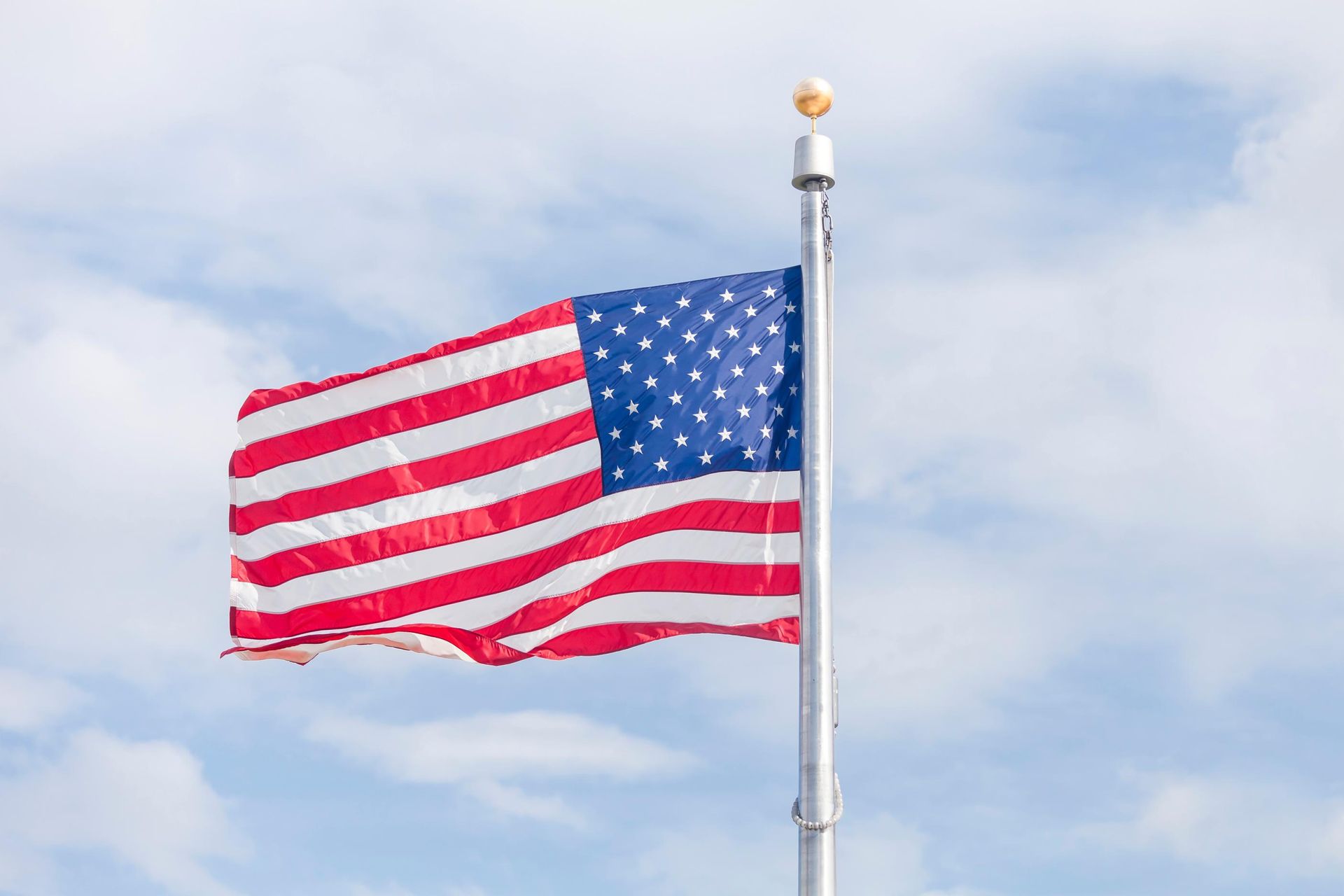 American flag waving on a pole against a cloudy sky.
