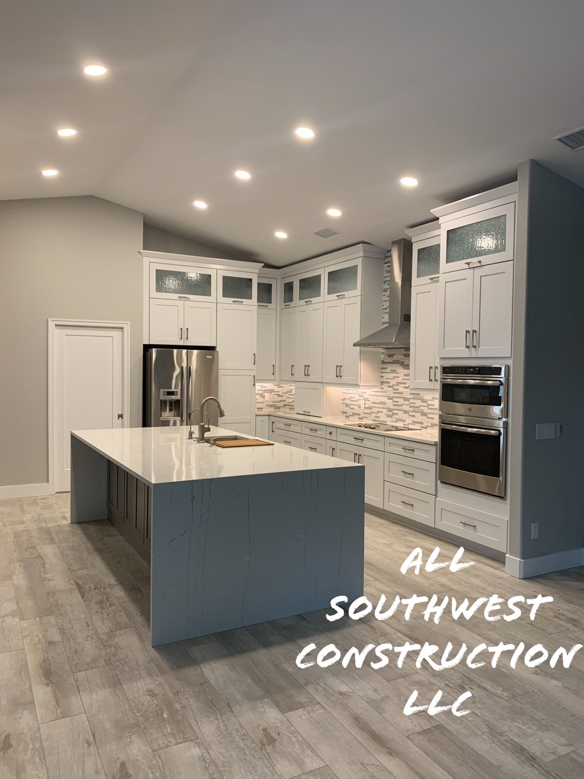 Modern kitchen with white cabinets, island, stainless appliances, and light wood-look flooring.