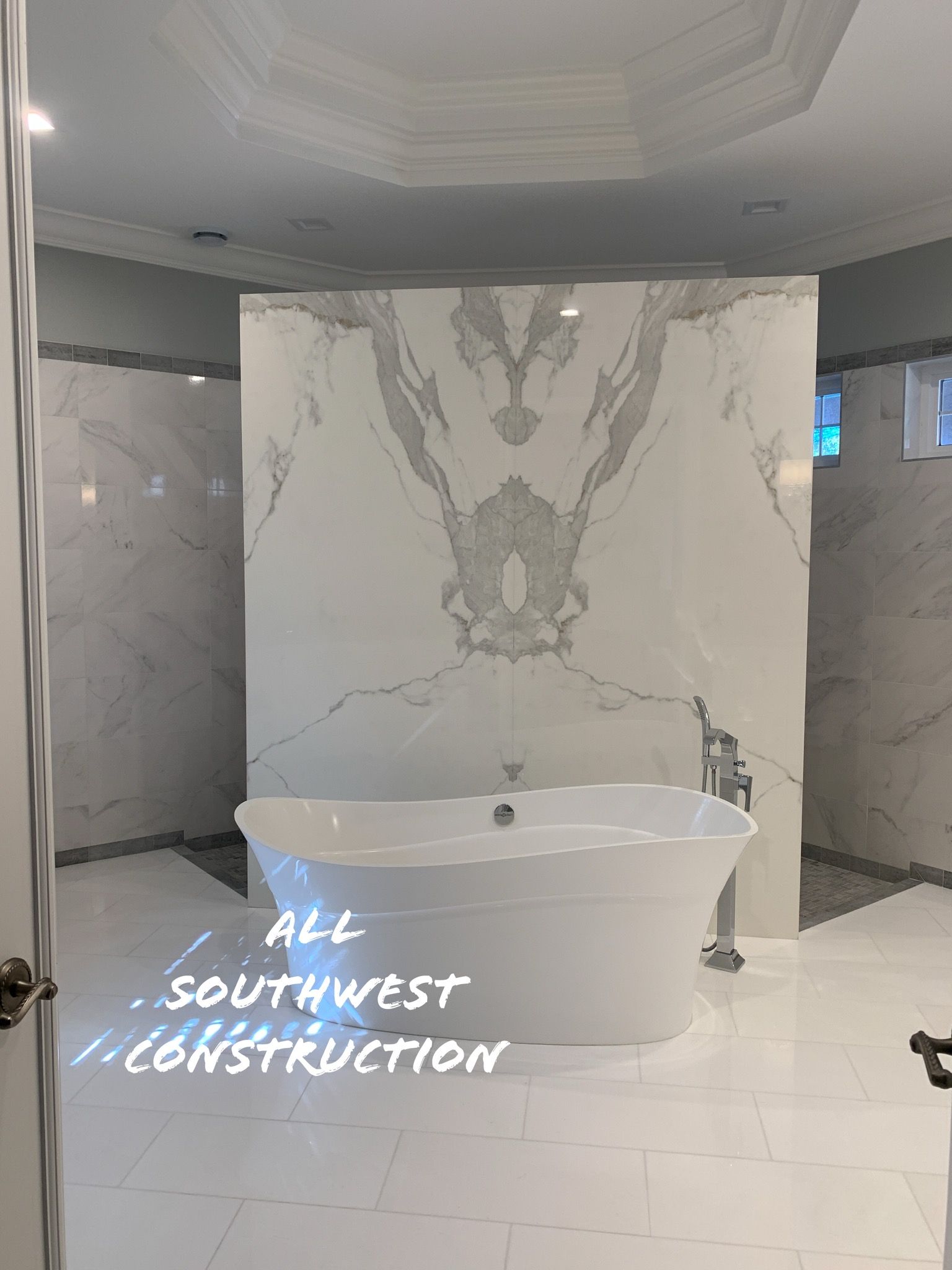 Luxurious bathroom with white freestanding tub and marble accent wall.
