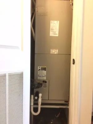 A gray HVAC air handler unit standing inside a closet with white louvered doors.