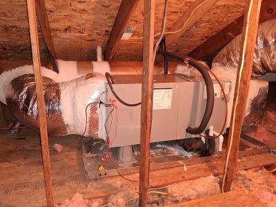 HVAC air handler unit installed in an attic space, connected to insulated ducts and resting on a wooden platform.