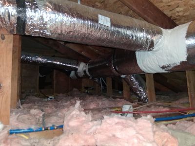 Attic space showing exposed wooden rafters, pink insulation, and several silver-insulated HVAC ducts.