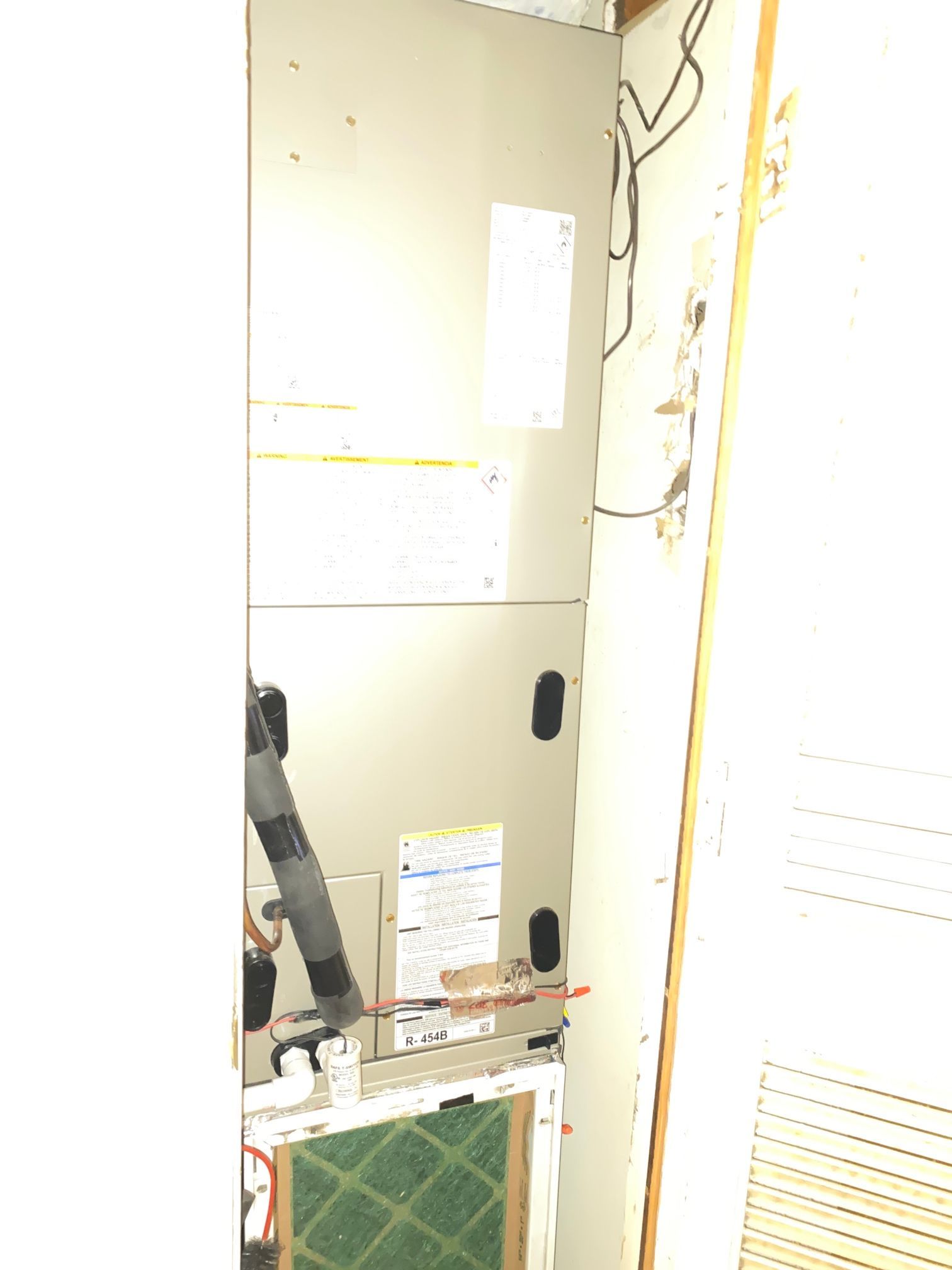 A vertical furnace unit installed in a closet with a visible air filter at the bottom and connected electrical wiring.