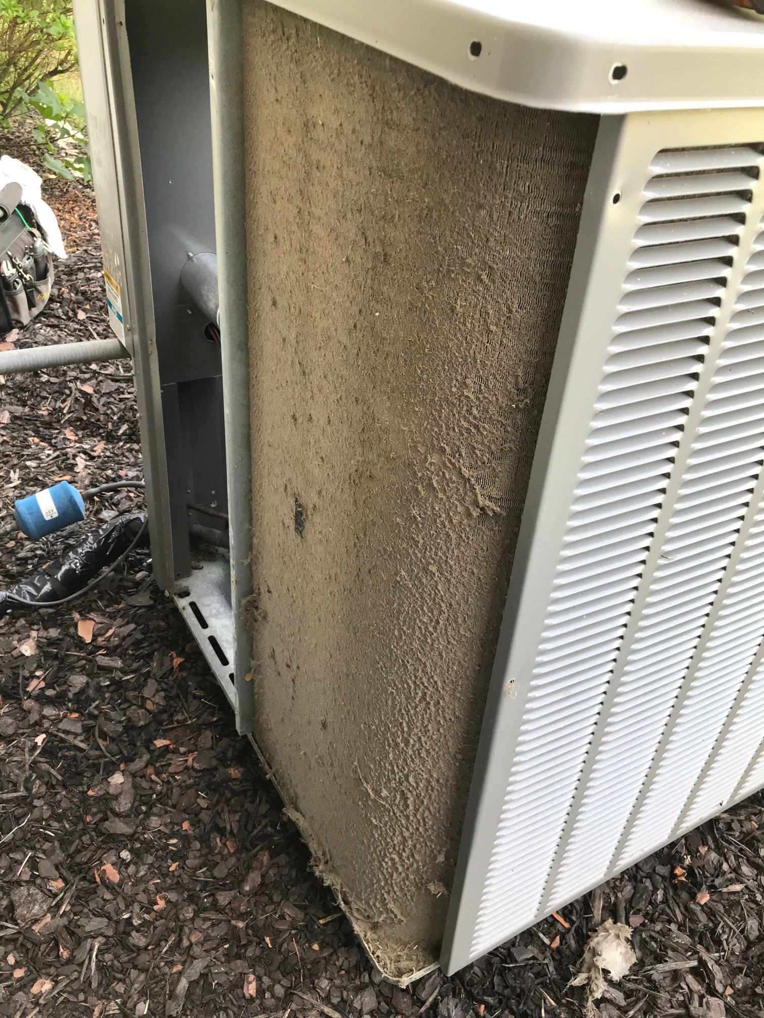 An outdoor air conditioner unit showing a heavily clogged, dusty cooling coil filter surface.