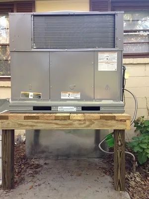 An outdoor HVAC unit sitting on a raised wooden platform structure outside a brick home.