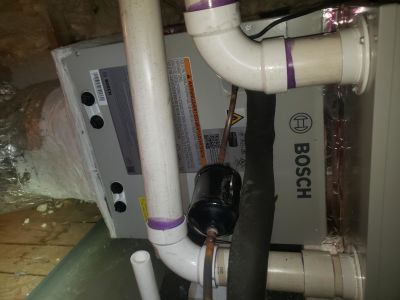 A Bosch HVAC air handler unit in an attic, showing white PVC plumbing, copper lines, and a black filter dryer.