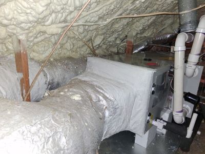 An HVAC air handler unit with attached ductwork in an attic space insulated with yellow spray foam.