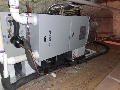 A grey Bosch HVAC air handler unit installed in an attic space with connected piping, wiring, and insulation.