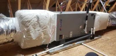 An attic-installed Trane air handler unit connected to insulated ductwork, resting on a metal platform.