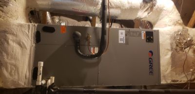 A gray Gree HVAC air handler unit installed in a dark attic space with insulated ductwork.