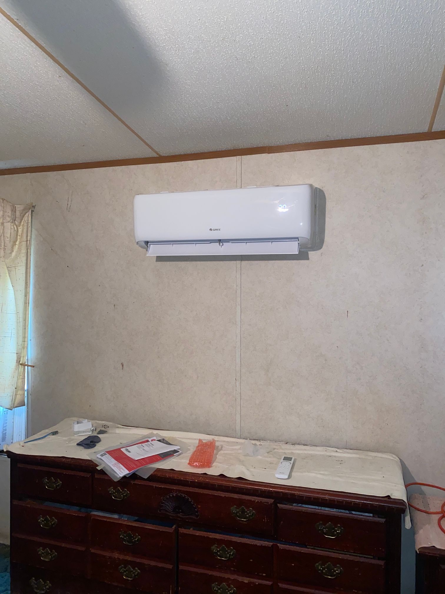 A white wall-mounted air conditioner unit positioned above a wooden dresser in a room with patterned wallpaper.