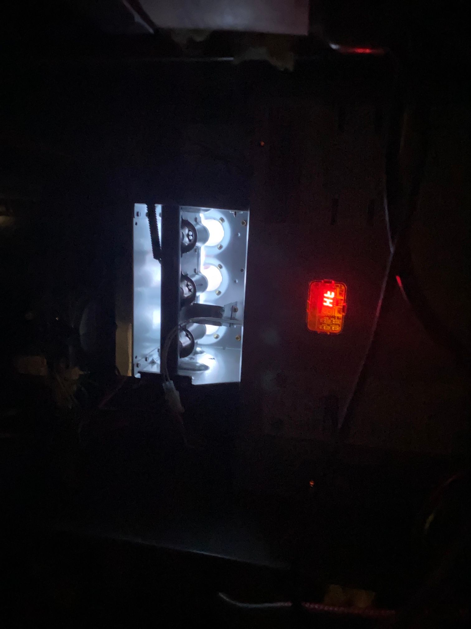 A dark view of a furnace interior showing glowing white burners and a small, rectangular red status indicator light.