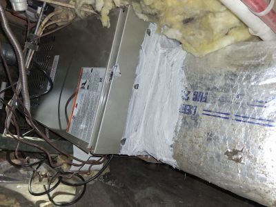 HVAC air handler unit connected to insulated ductwork with white sealant in a cluttered crawl space.