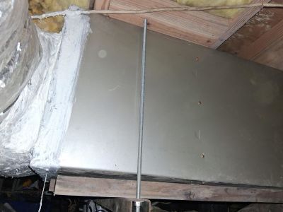 A metal HVAC duct suspended by a threaded rod in an attic, with insulated flexible ducting visible on the left.