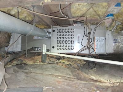 HVAC air handler unit mounted in a crawl space with exposed insulation, wiring, and ductwork.