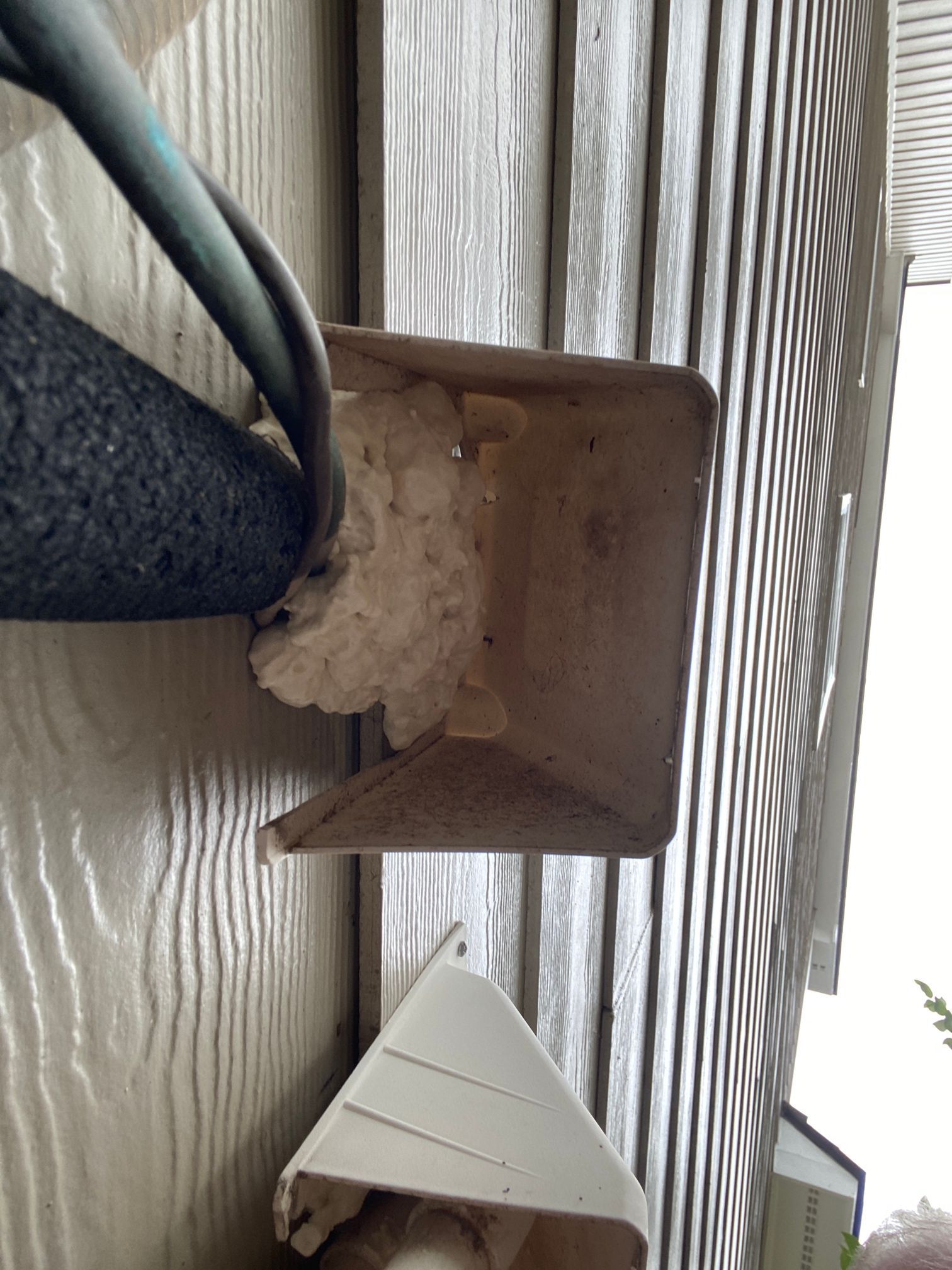 A utility pipe covered in black foam insulation exits a building wall, partially sealed with expanding spray foam.