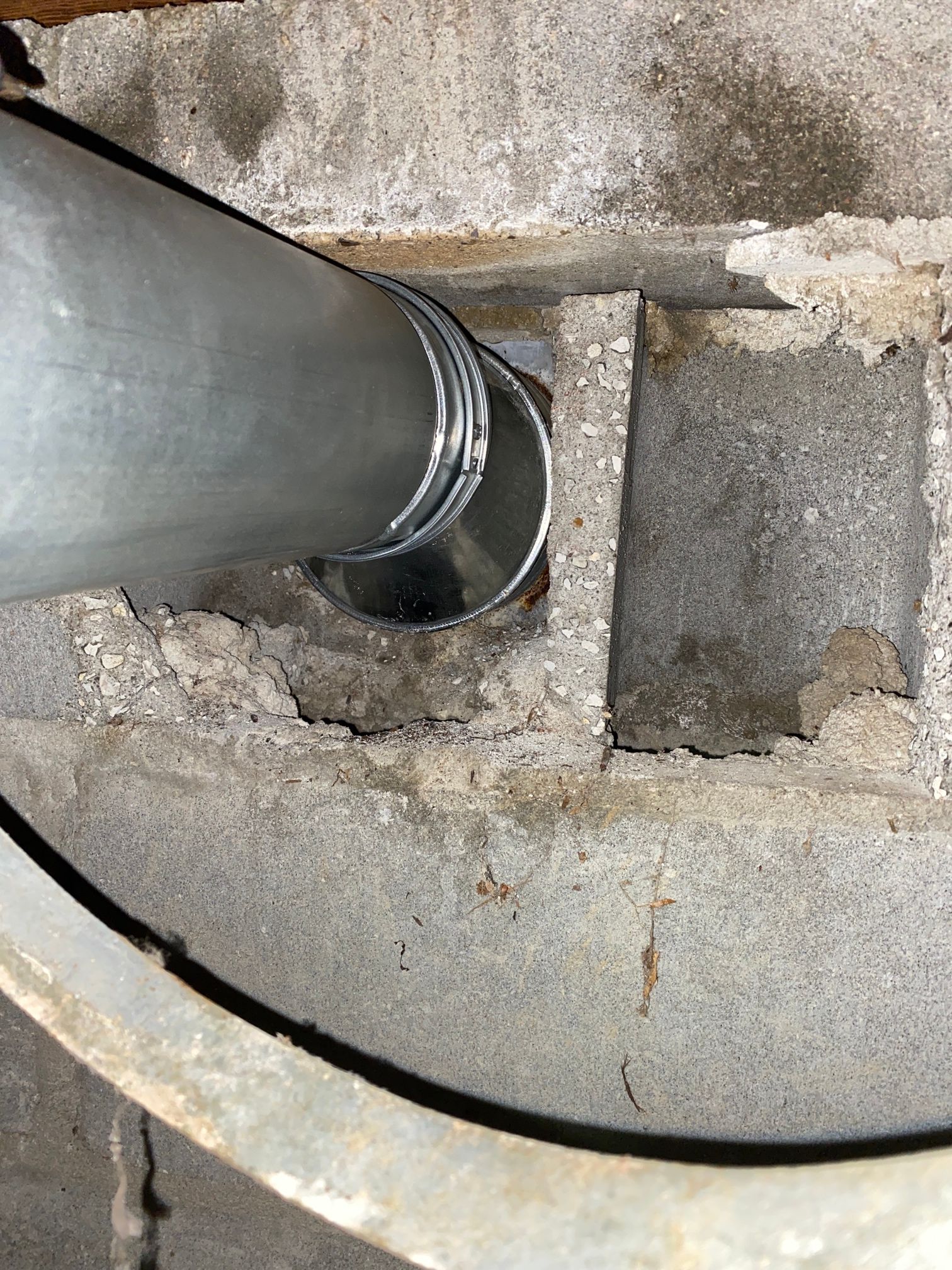 A metal pipe enters a hole in a gray concrete block, showing an unsealed connection with surrounding debris.