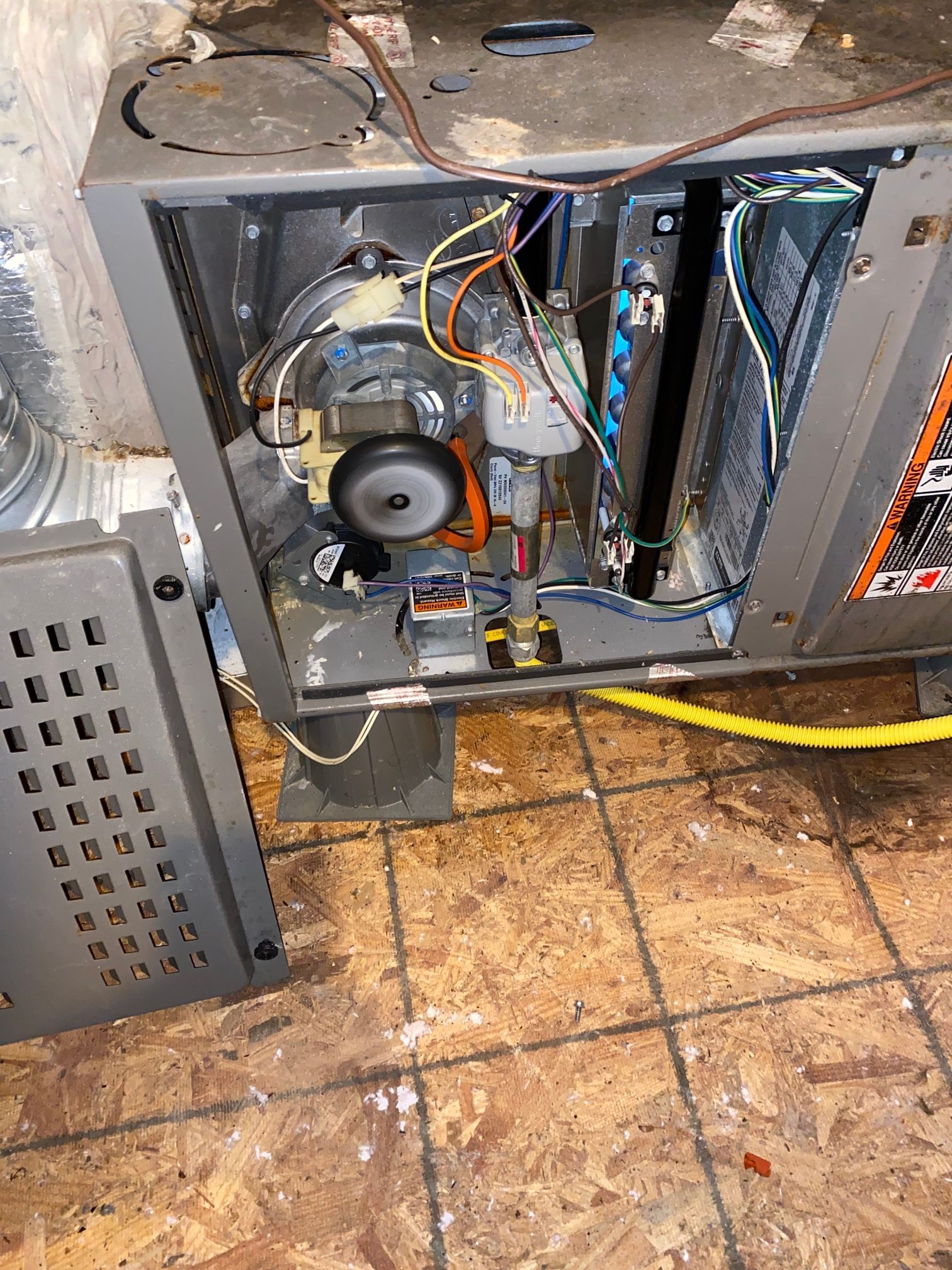 An open gray furnace interior with exposed wiring, a circular fan motor, and a detached metal access panel on the floor.