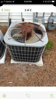 An outdoor residential HVAC air conditioner unit with a rusty fan guard, situated on a ground pad near a gas meter.