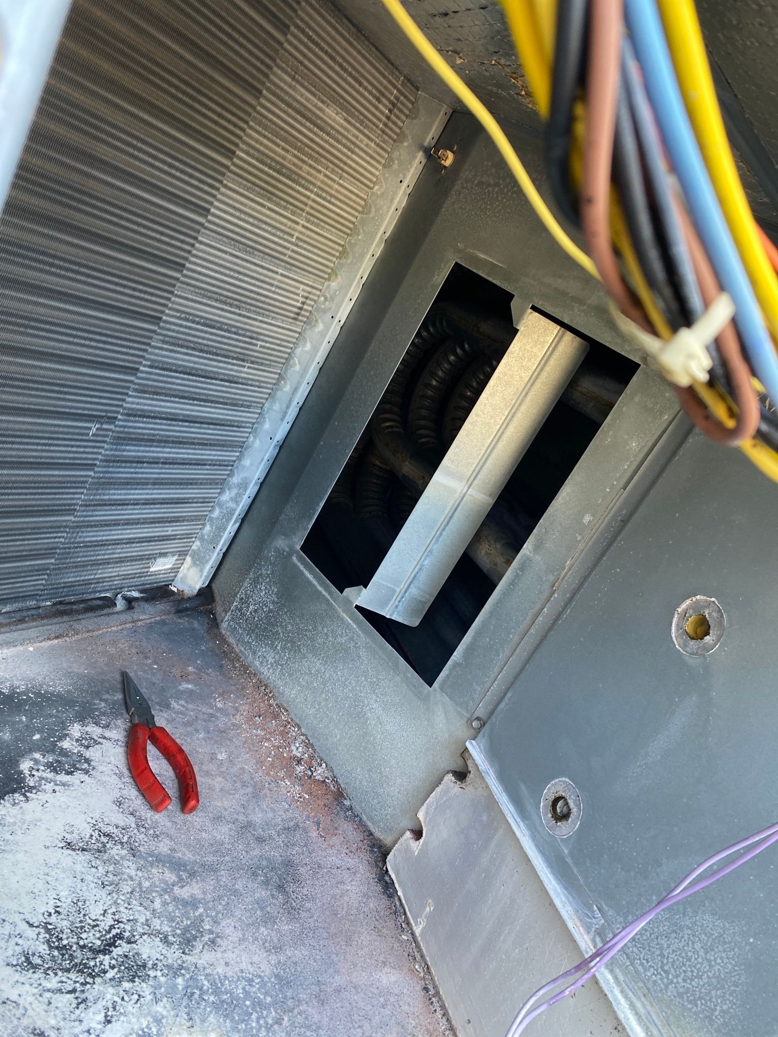 Interior view of an HVAC air handler unit showing wiring, metal ductwork, and small red pliers resting on the bottom.