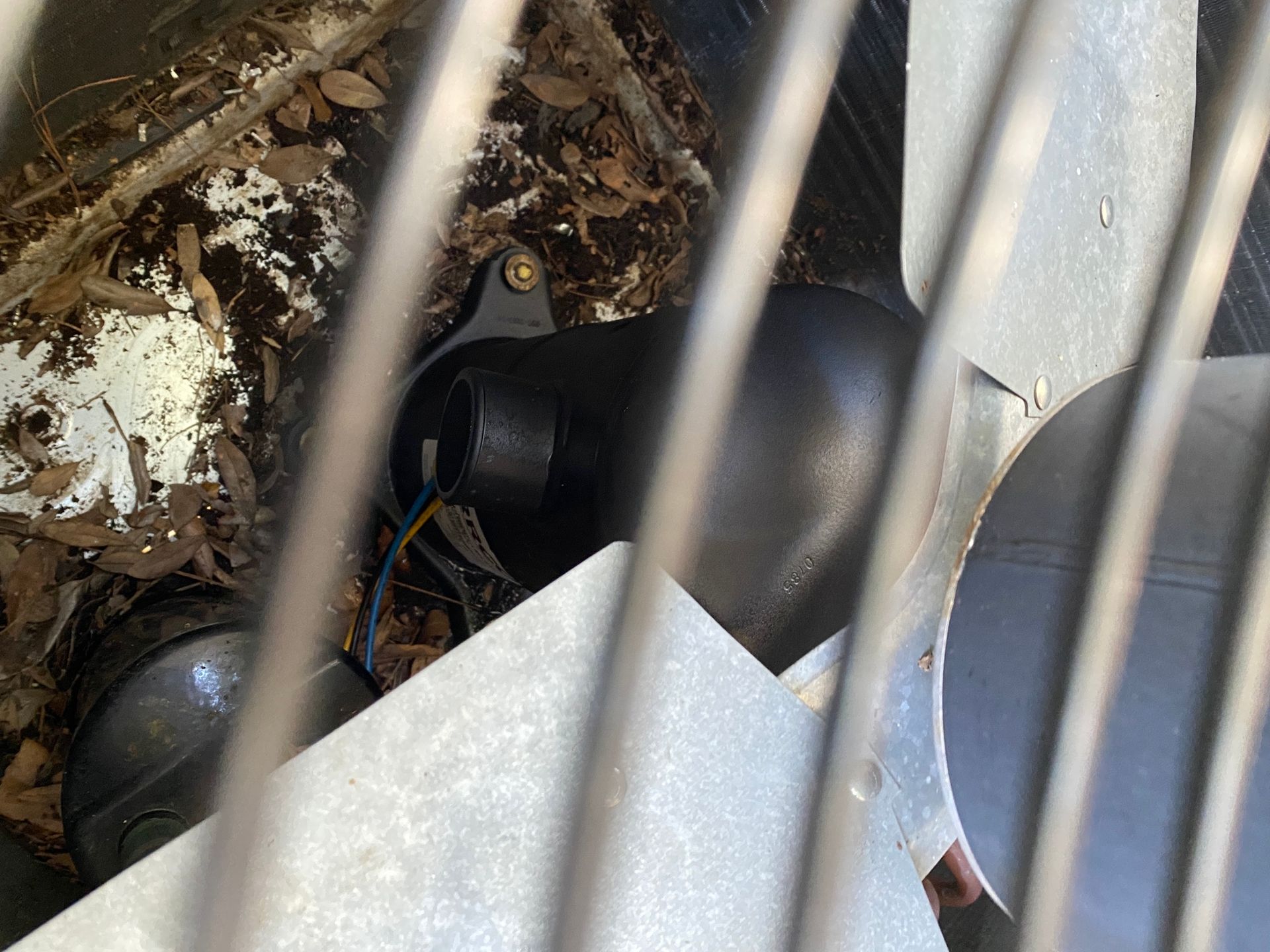 The interior of an outdoor AC unit showing a black compressor, a fan blade, and debris on the base panel.