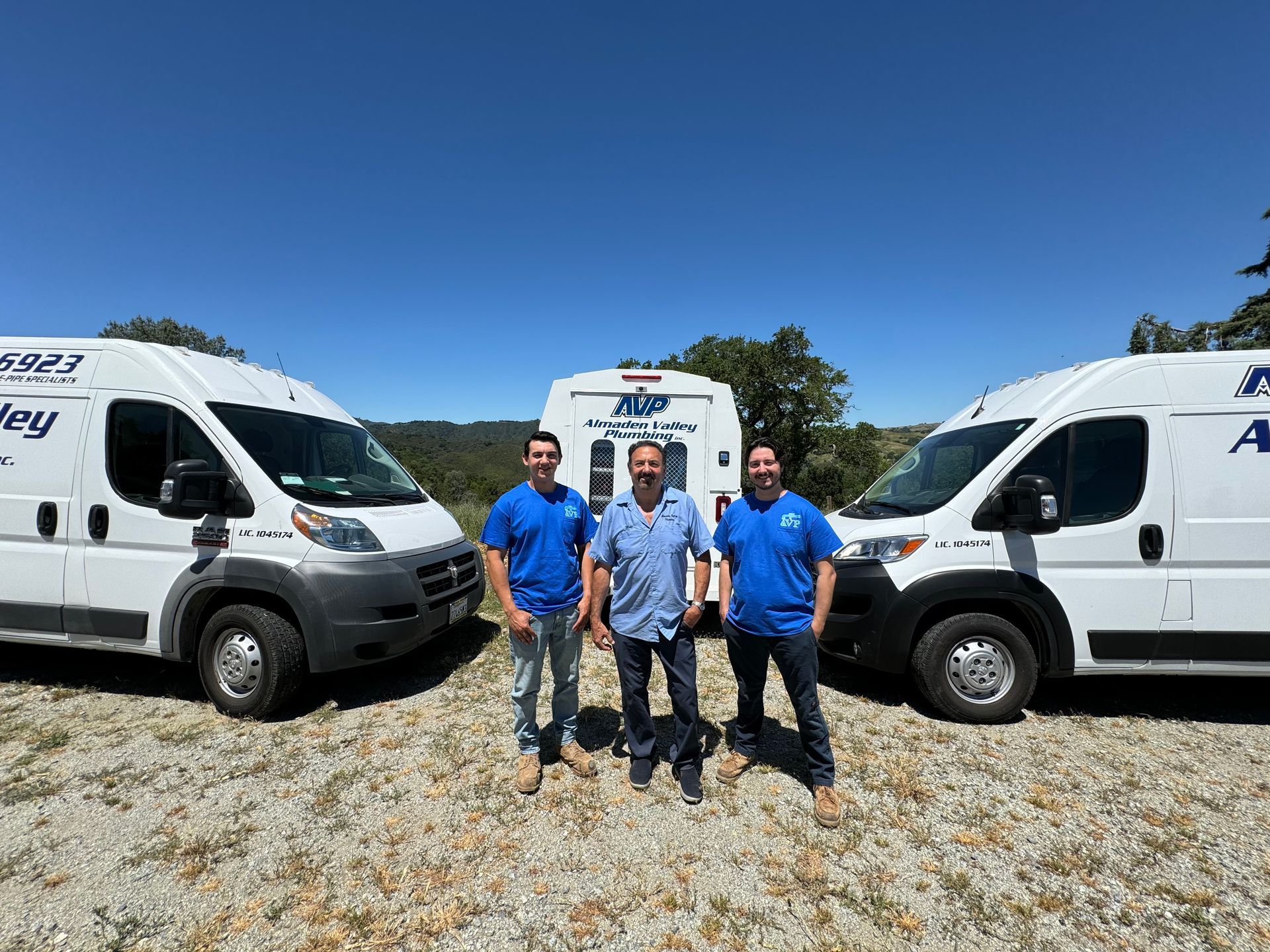 Three men are posing for a picture in front of three vans.