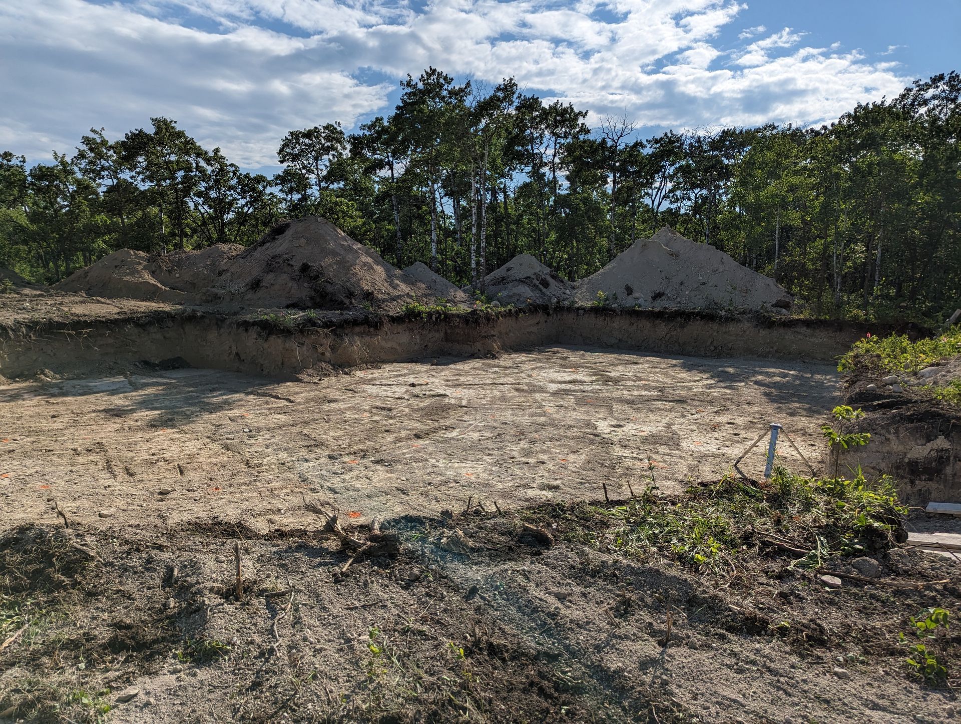 A large pile of dirt is sitting in the middle of a field surrounded by trees.