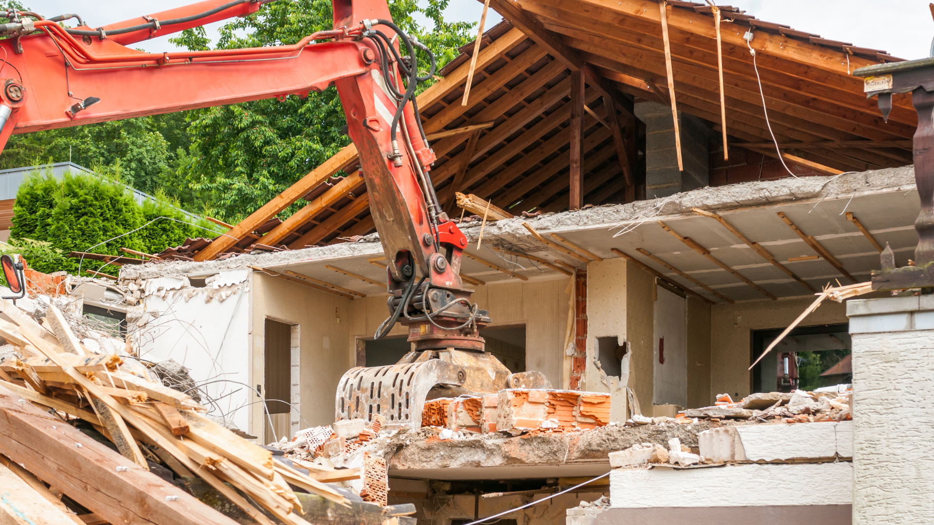 A large red excavator is demolishing a house.
