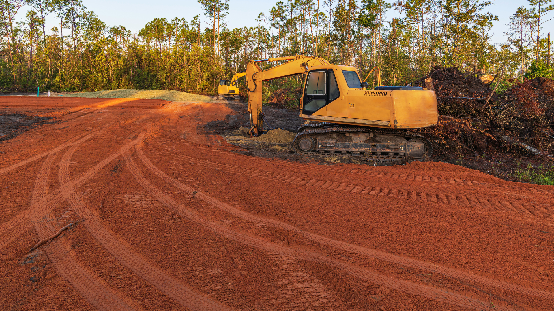 A yellow excavator is working on a dirt road.