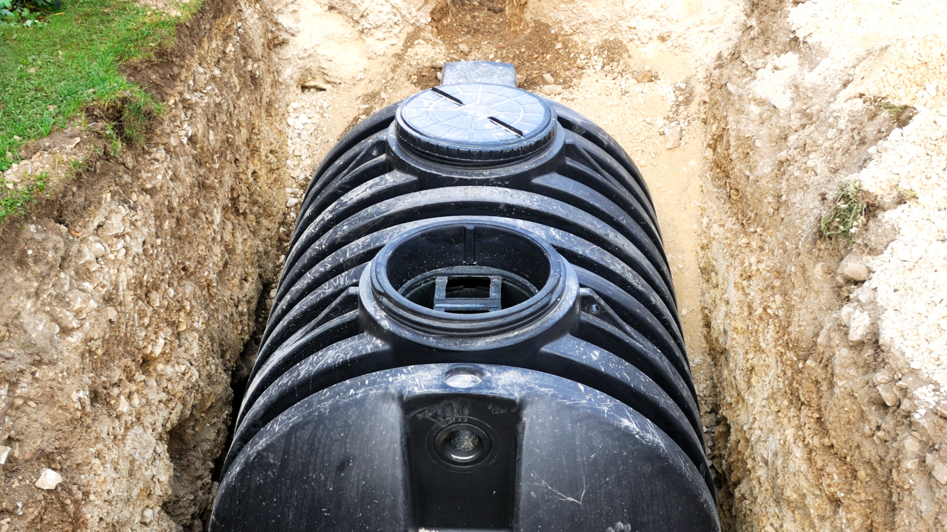 A large black septic tank is sitting in a trench.