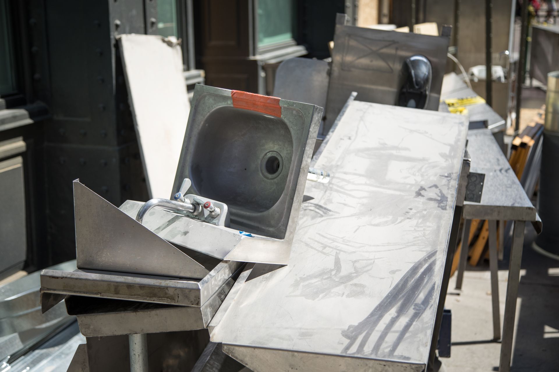 A stainless steel sink and industrial countertop sections stacked outdoors on a city sidewalk.