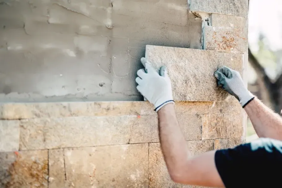 Gloved hands applying cement plaster to a brick wall outdoors
