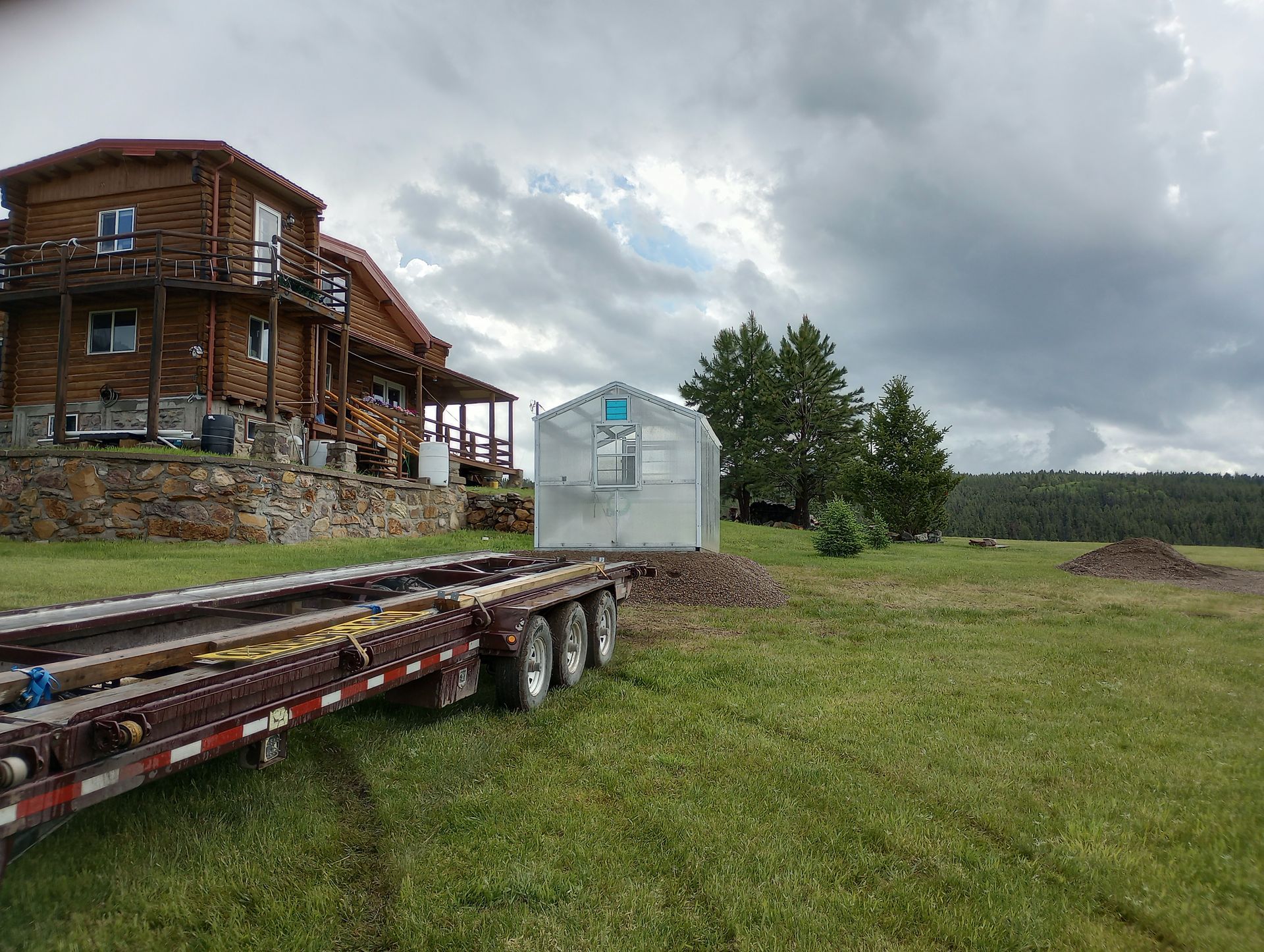 A trailer is parked in a grassy field in front of a house.