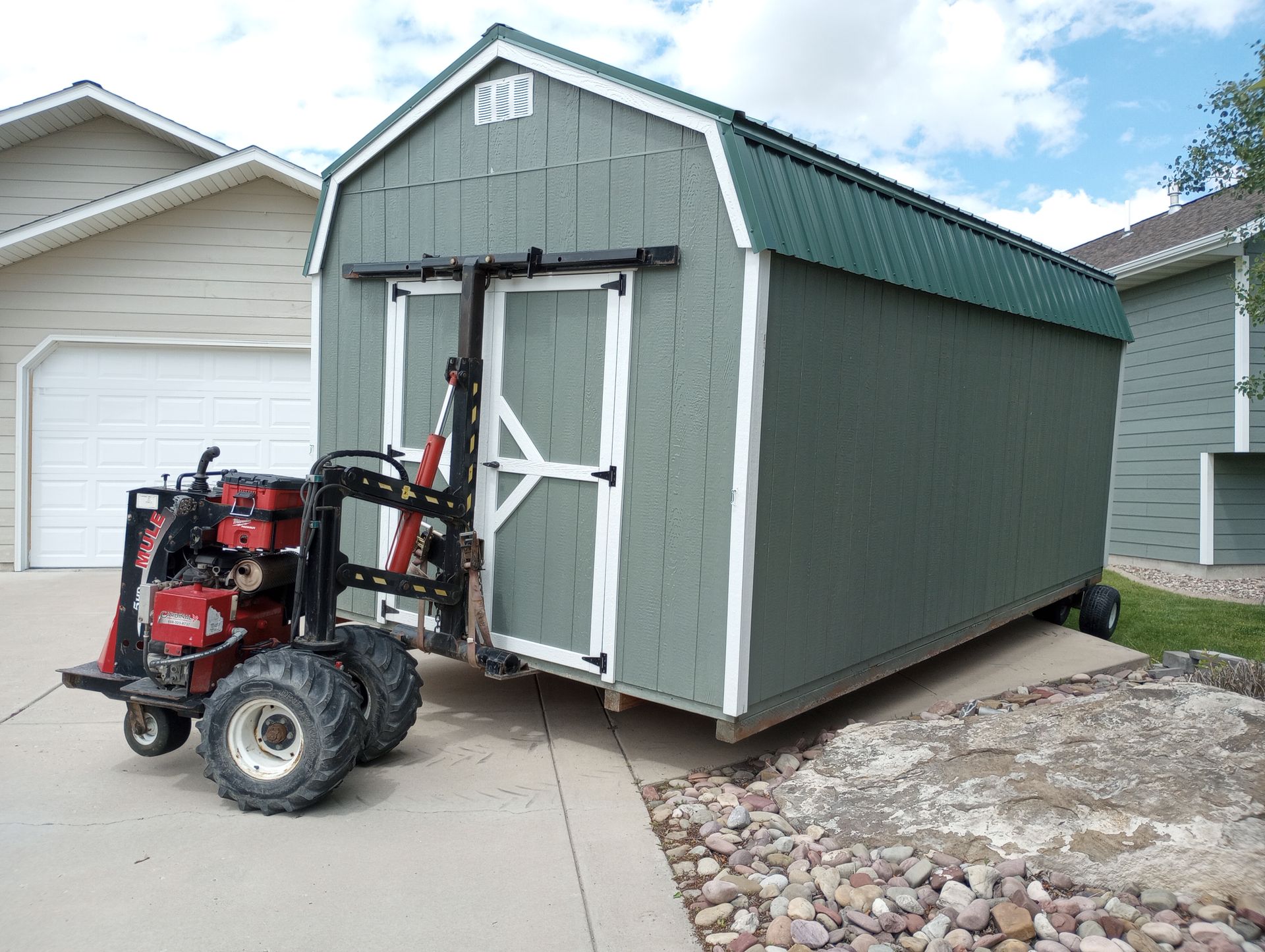 A shed is being lifted by a forklift in a driveway.