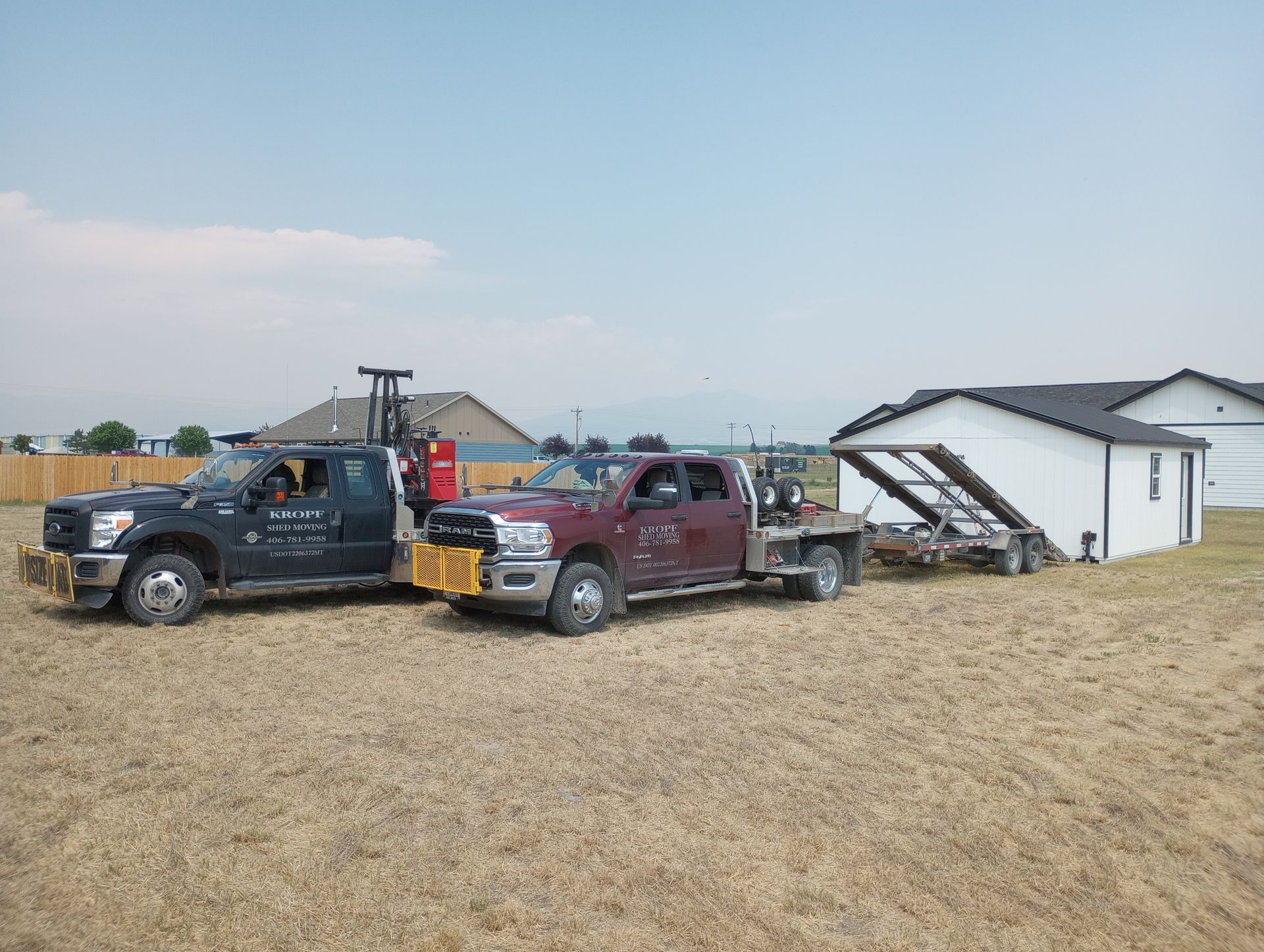 Two tow trucks are parked in a field next to a house.