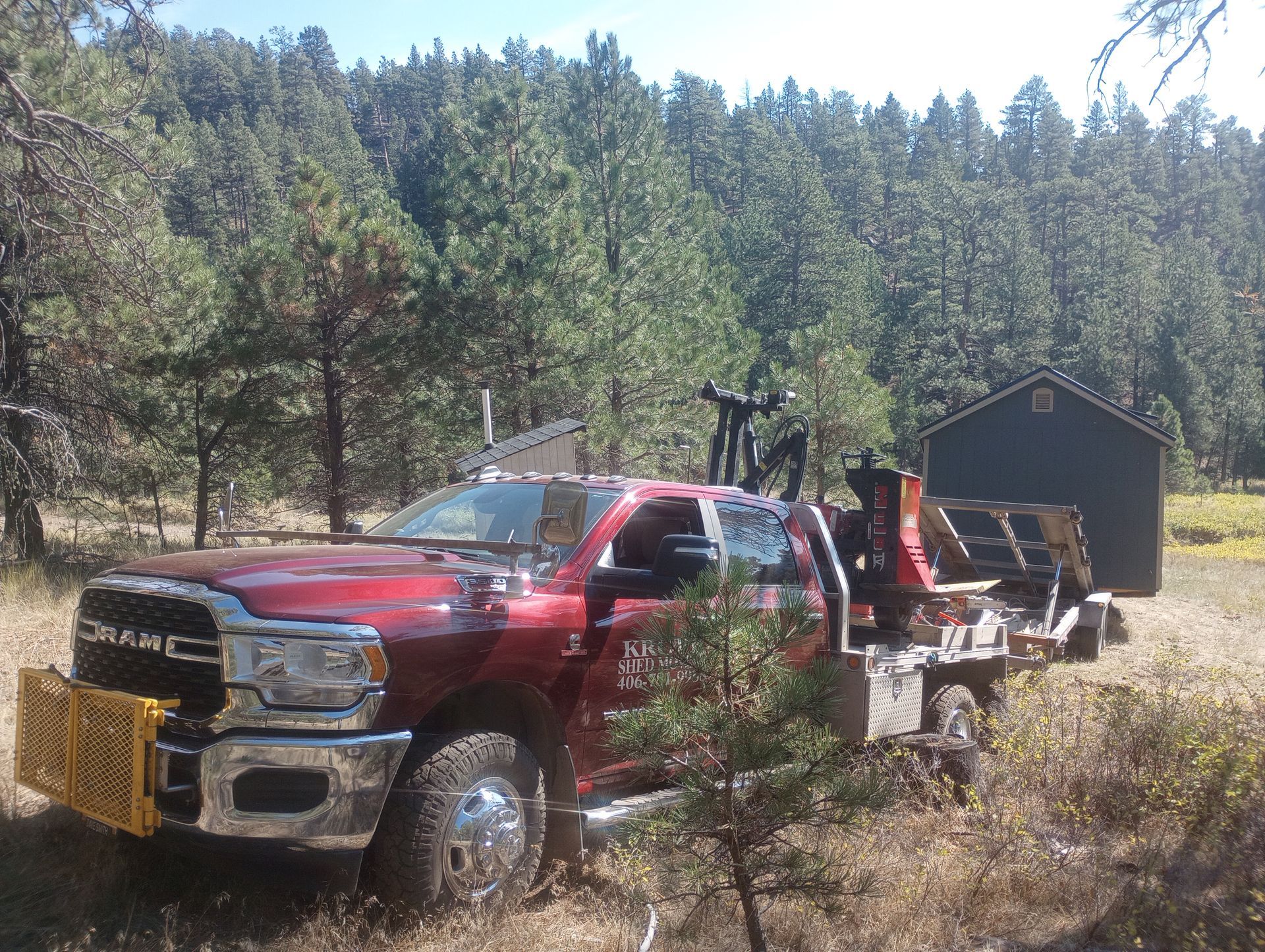 A red ram truck is parked in a field with trees in the background