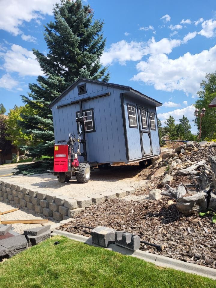 A blue shed is being moved by a red forklift.