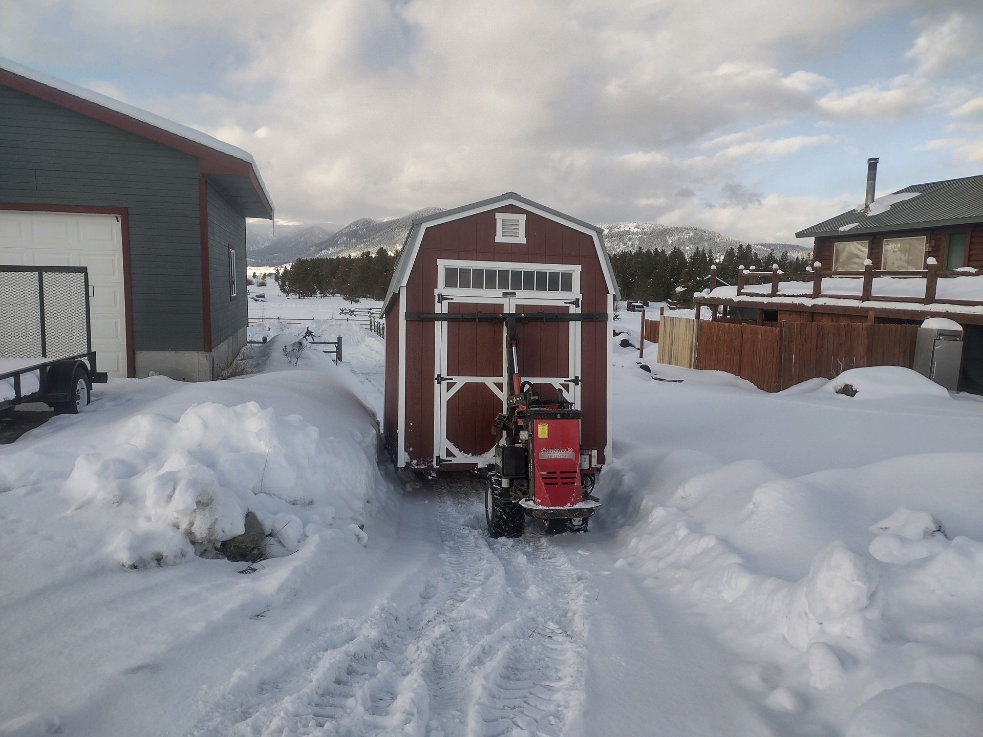A red barn is being pulled by a tractor in the snow