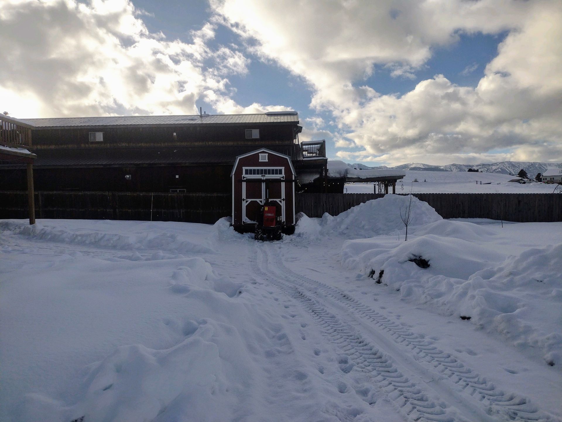 A snow blower is clearing snow in front of a barn