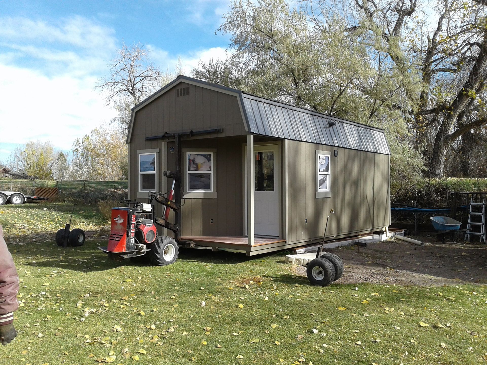 A shed is being moved by a forklift in a grassy field.