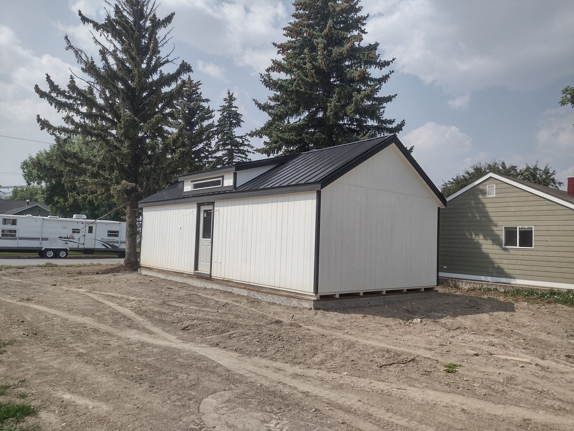 A small white building with a black roof is in a dirt field