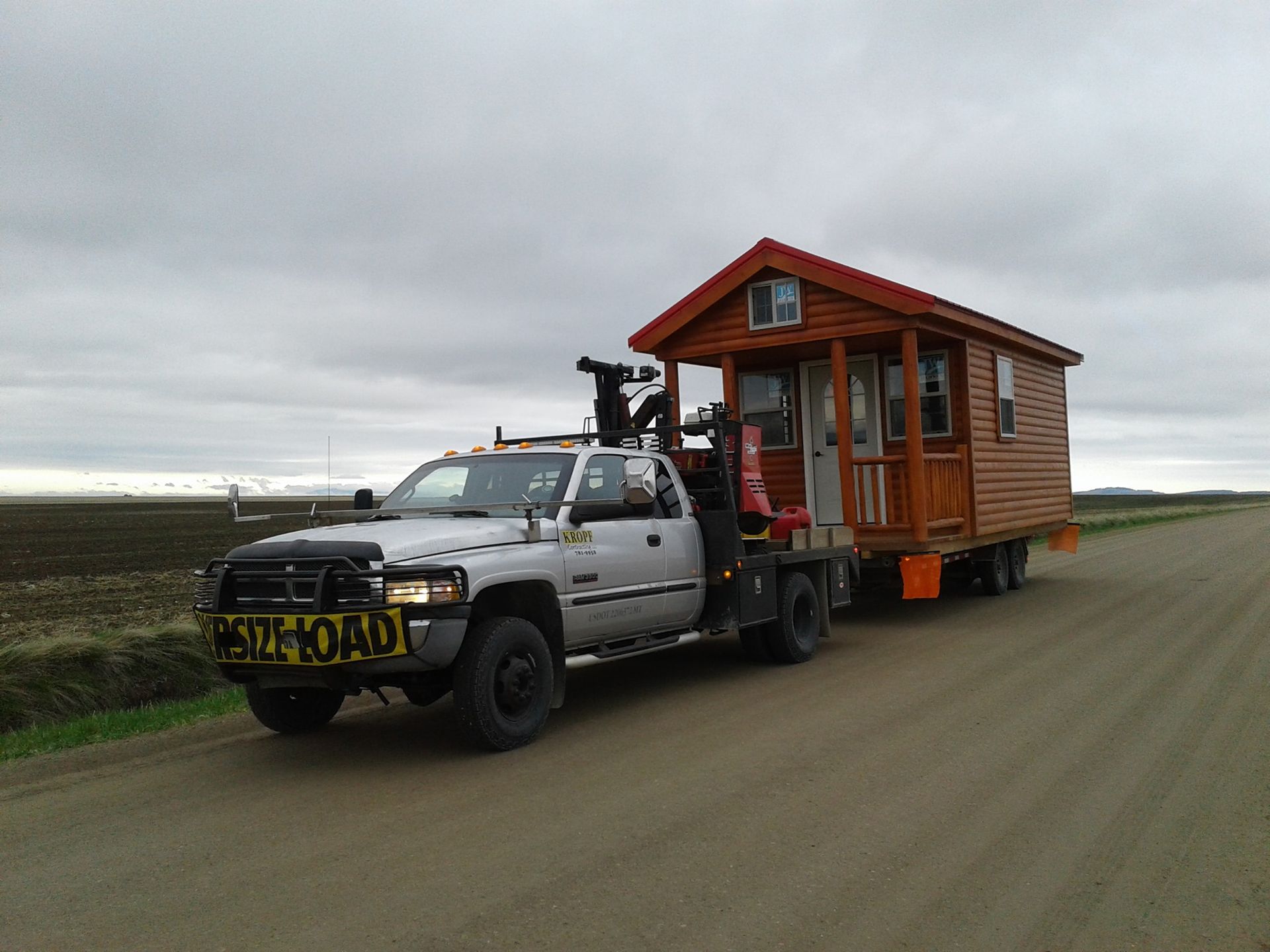 A tow truck is pulling a small house down a dirt road