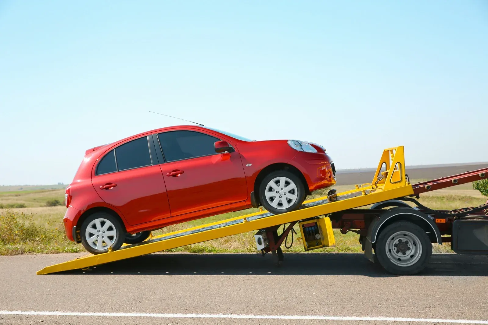 Red car being towed onto a yellow flatbed tow truck on a road.
