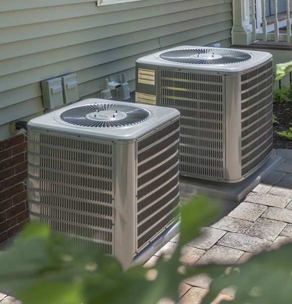 Two air conditioners are sitting on the side of a house.
