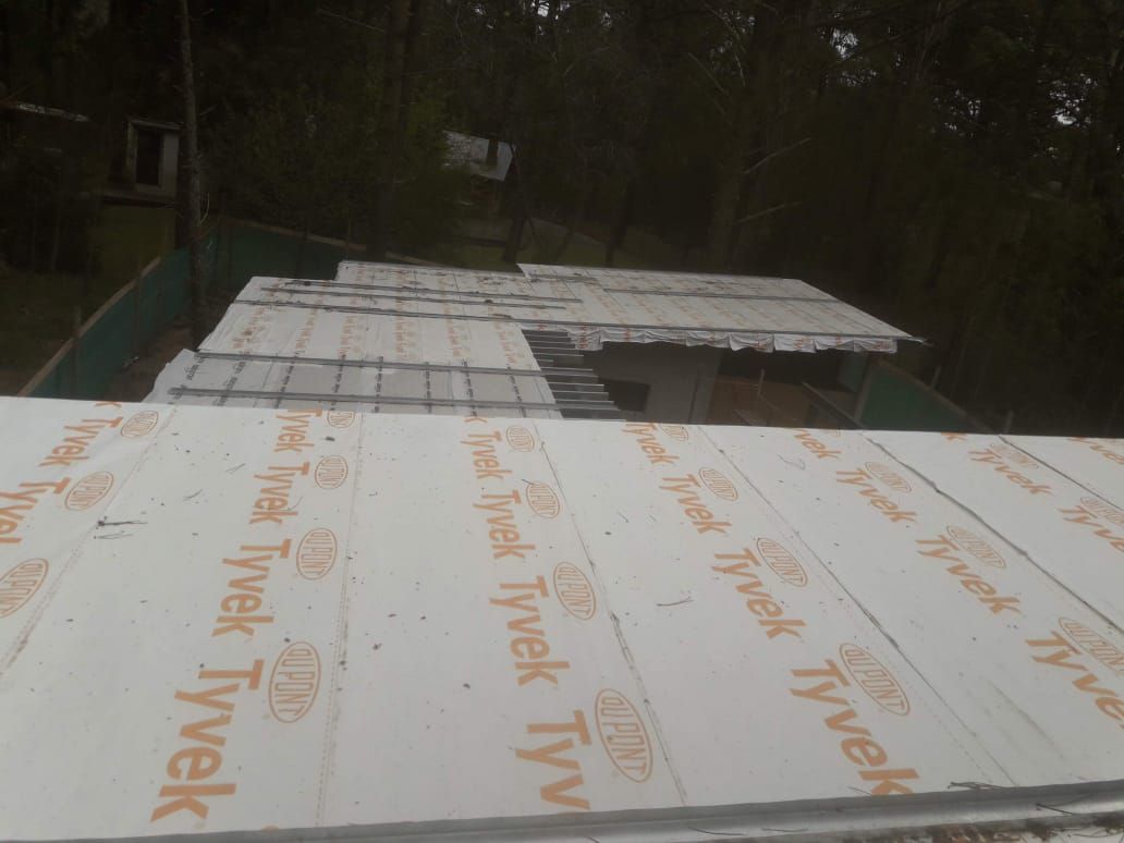 Techo con base de Tyvek blanco. Techo metálico distante bajo árboles.