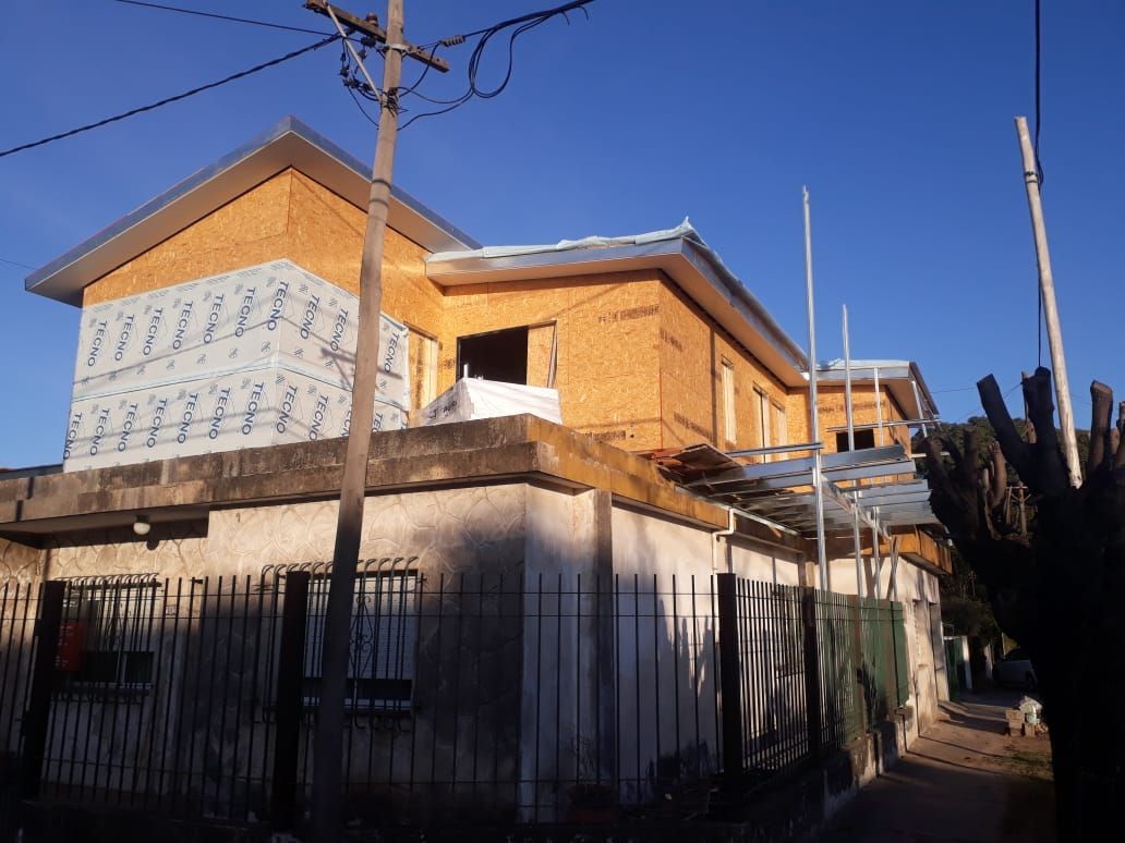 Casa de dos plantas de ladrillo en construcción, con aislamiento visto y edificio de techo plano al frente.
