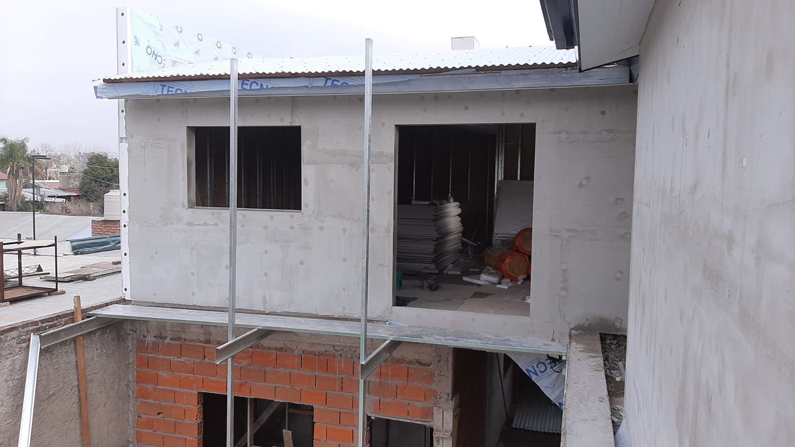 Edificio en construcción con paredes sin terminar, ventanas abiertas y andamios.