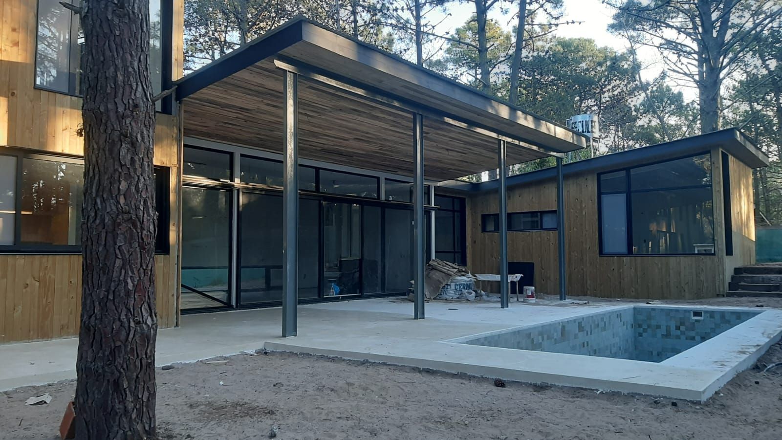 Casa moderna con revestimiento de madera, grandes ventanales y un patio cubierto con vista a una pequeña piscina.